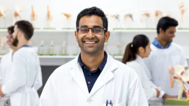 Scientist in lab coat smiling in laboratory with anatomical models.