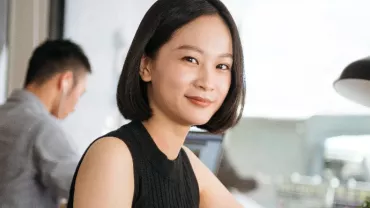 An Asian woman in a sleeveless top smiling to the camera in an office setting