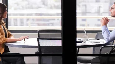 Two people engaged in a discussion at a round table in an office setting.