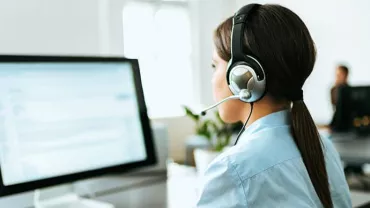 Person at a desk wearing a headset, working on a computer in an office.