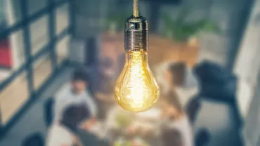 A glowing light bulb above a group of people in a meeting room.