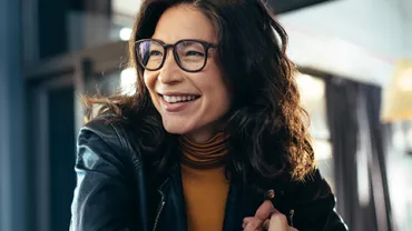 A person smiling while holding a cup, seated in a cozy indoor setting.