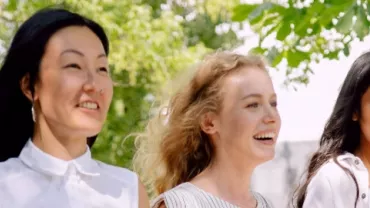 Three people walking outdoors, smiling under the trees.