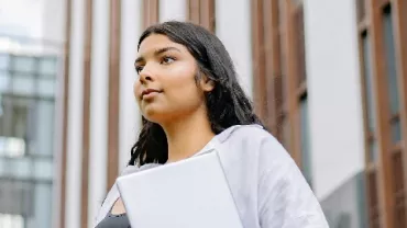 Person holding books, walking near a modern building.