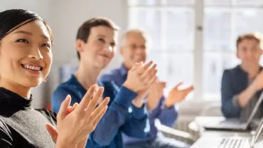 People sitting in a meeting room clapping and smiling.