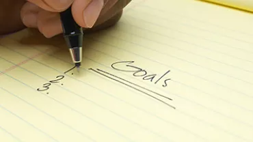 Handwriting goals on a yellow notepad.