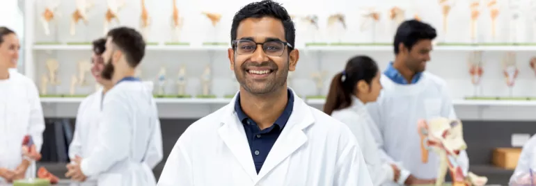 Scientist in lab coat smiling in laboratory with anatomical models.