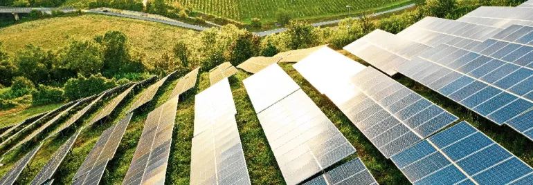 Solar panels in a field with green hills and trees in the background.